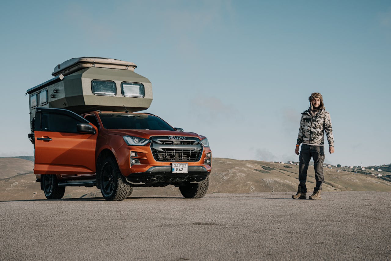 Man standing by an orange SUV with camper cabin in Ordu, Türkiye's scenic hills.